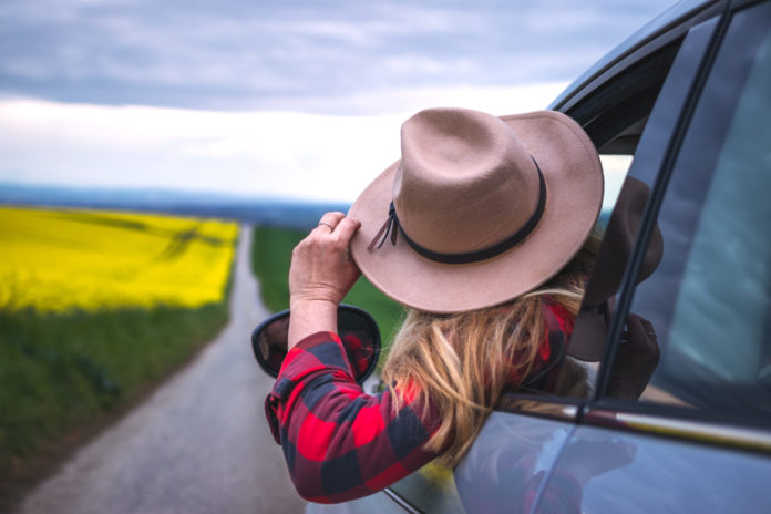 Woman driver with hat looking from car window outside. Travel and transportation concept