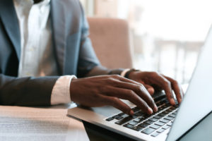 Businessman working on laptop with some documents on table. Close up on male hands typing on laptop keyboard.